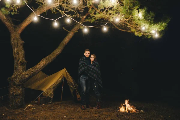 Aşık genç bir çift, ormanda bir çadırın önünde eski bir çelenkle kamp kuruyor. Çok gürültülü bir fotoğraf, seçici bir odak noktası var.