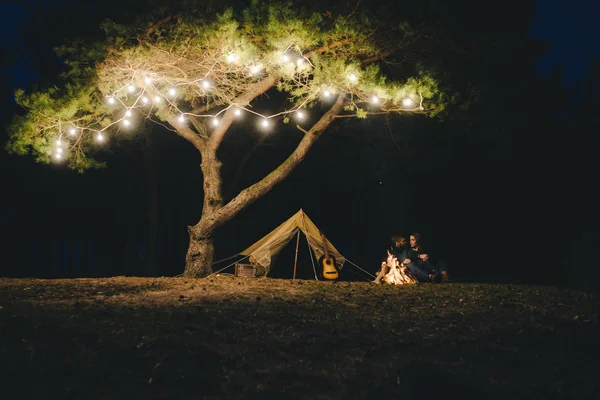 Aşık genç bir çift, ormanda bir çadırın önünde eski bir çelenkle kamp kuruyor. Çok gürültülü bir fotoğraf, seçici bir odak noktası var.