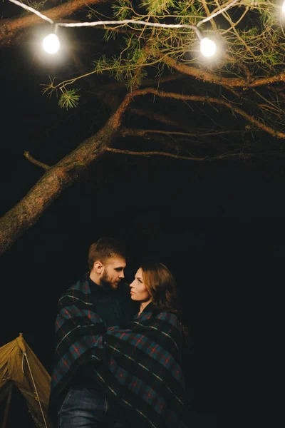 Aşık genç bir çift, ormanda bir çadırın önünde eski bir çelenkle kamp kuruyor. Çok gürültülü bir fotoğraf, seçici bir odak noktası var.