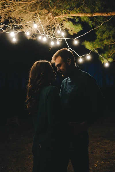 Aşık genç bir çift, ormanda bir çadırın önünde eski bir çelenkle kamp kuruyor. Çok gürültülü bir fotoğraf, seçici bir odak noktası var.