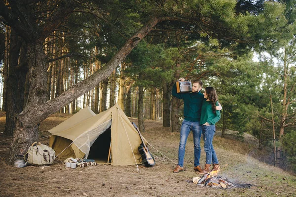 Aşık genç bir çift, kamp yapan turistleri ormandaki bir çadırın önünde oturup retro radyo dinliyorlar.