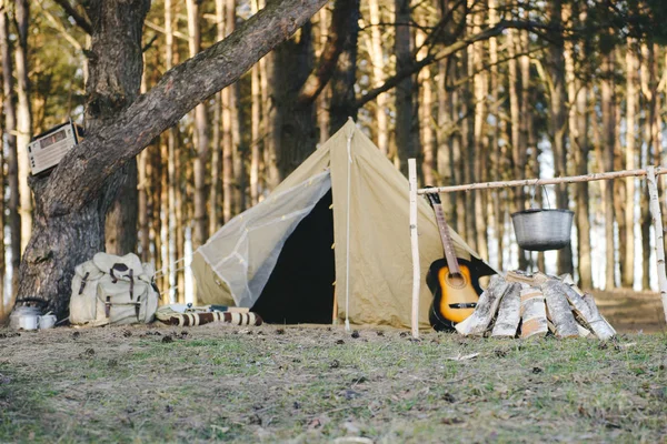 Retro çadır, sırt çantası, gitar, nehir kenarındaki ormanda yangın.