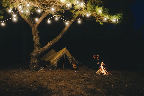 Aşık genç bir çift, ormanda bir çadırın önünde eski bir çelenkle kamp kuruyor. Çok gürültülü bir fotoğraf, seçici bir odak noktası var.