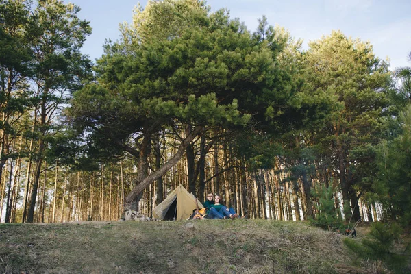 Genç aşıklar kamp yapıyor, kamp ateşinin yanında ormanın içinde çadırın karşısında oturuyorlar. 
