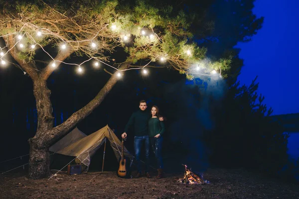 Aşık genç bir çift, ormanda bir çadırın önünde eski bir çelenkle kamp kuruyor. Çok gürültülü bir fotoğraf, seçici bir odak noktası var.
