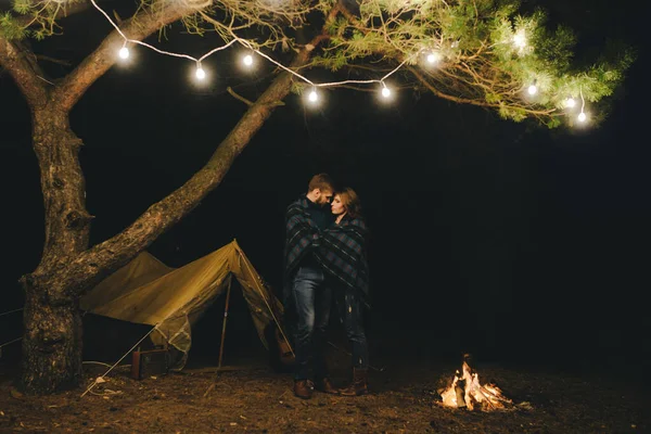 Aşık genç bir çift, ormanda bir çadırın önünde eski bir çelenkle kamp kuruyor. Çok gürültülü bir fotoğraf, seçici bir odak noktası var.