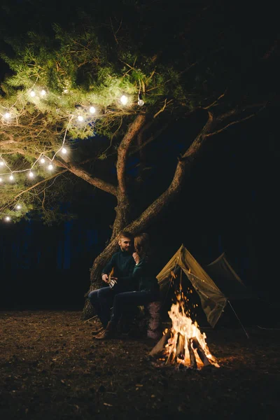 Aşık genç bir çift, ormanda bir çadırın önünde eski bir çelenkle kamp kuruyor. Çok gürültülü bir fotoğraf, seçici bir odak noktası var.