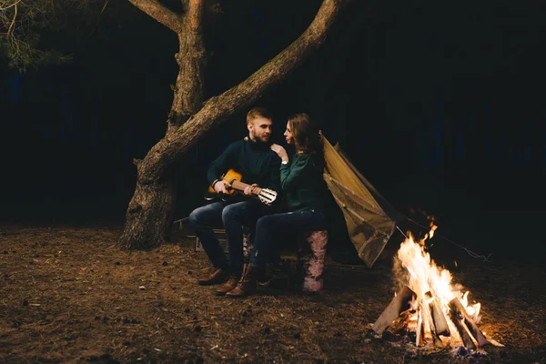 Aşık genç bir çift, ormanda bir çadırın önünde eski bir çelenkle kamp kuruyor. Çok gürültülü bir fotoğraf, seçici bir odak noktası var.
