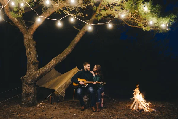 Aşık genç bir çift, ormanda bir çadırın önünde eski bir çelenkle kamp kuruyor. Çok gürültülü bir fotoğraf, seçici bir odak noktası var.