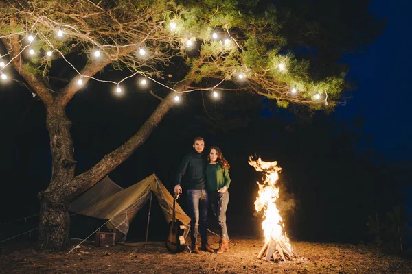Aşık genç bir çift, ormanda bir çadırın önünde eski bir çelenkle kamp kuruyor. Çok gürültülü bir fotoğraf, seçici bir odak noktası var.