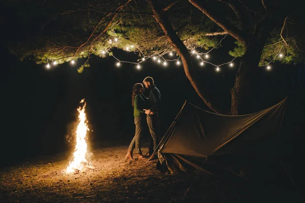 Aşık genç bir çift, ormanda bir çadırın önünde eski bir çelenkle kamp kuruyor. Çok gürültülü bir fotoğraf, seçici bir odak noktası var.