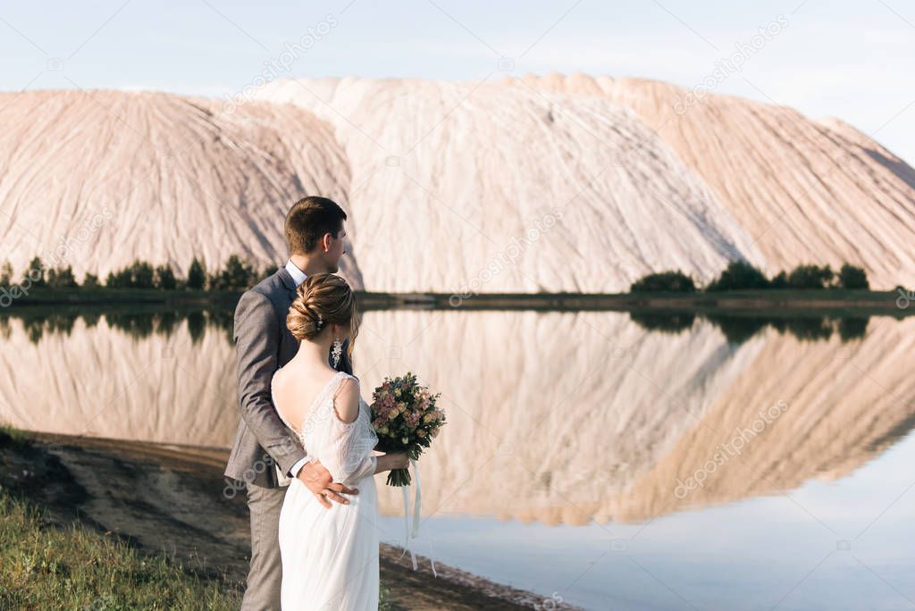 beautiful wedding couple hug each other and looking on mountain lake landscape