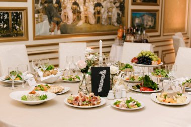 Yuvarlak beyaz masa büyük miktarda yiyecek ve çeşitli atıştırmalıklarla dolu. Lüks bir iç mekan, güzel bir servis.