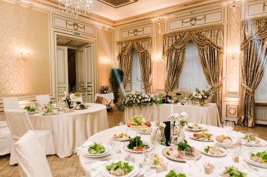 Yuvarlak beyaz masa büyük miktarda yiyecek ve çeşitli atıştırmalıklarla dolu. Lüks bir iç mekan, güzel bir servis.