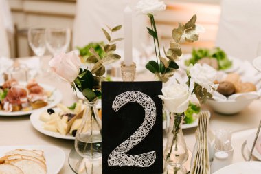 Yuvarlak beyaz masa, aperatifler lüks bir iç mekanda, masa ayarları, masa numarası kartı ve çiçekler, seçici odak