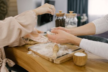 Bir erkek ve bir kızın elleri hamuru hazırlıyor. Ahşap bir arka planda merdaneli un. Seçici odak
