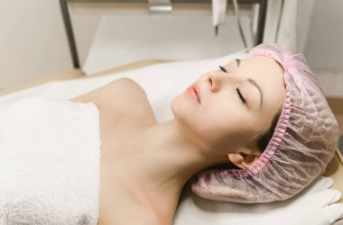 Kozmetik ve estetik cerrahının resepsiyonundaki çekici bir kızın yakın plan portresi, kozmetoloji, kırışıklık giderme, yüz masajı.