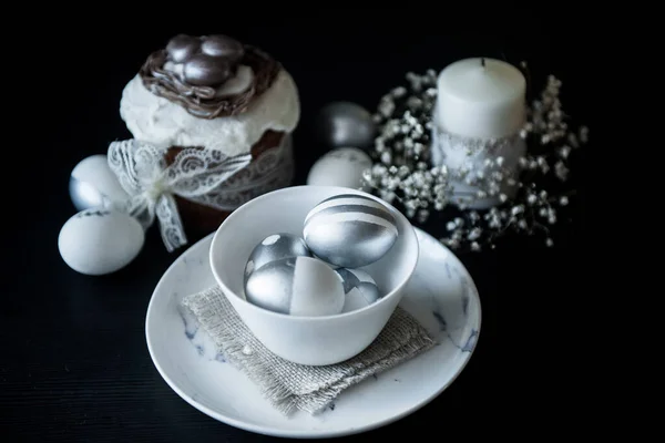 Traditional Easter cake with silver painted eggs, candles and willow on a black background. Selective focus