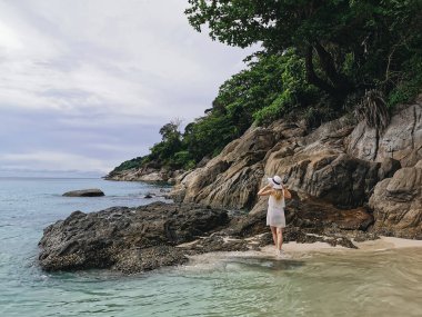 Mavi denizin kıyısında şapkalı ve gözlüklü çekici bir kız tatilin tadını çıkarıyor ve Tayland 'da kayalarla dolu vahşi bir sahilde seyahat ediyor.