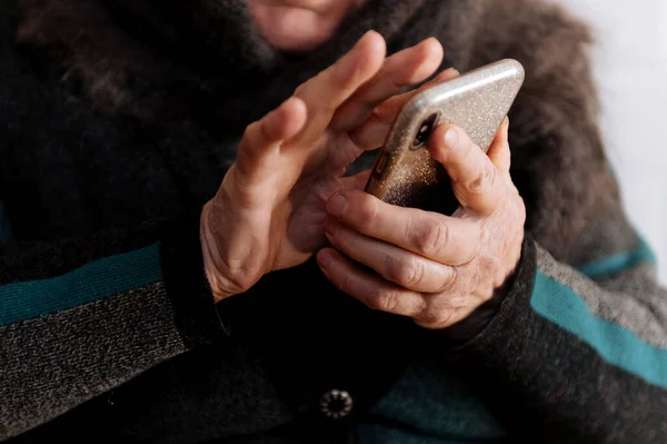 An elderly grandmother holds a mobile phone for the first time during the quarantine period of the coronavirus pandemic, close - up of hands