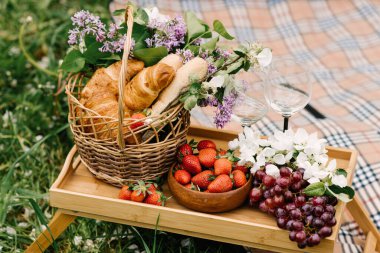 Bahçedeki yeşil çimlerin üzerinde çilek, üzüm ve çöreklerle piknik sepeti.