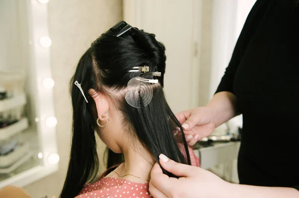 The hairdresser does hair extensions to a young girl in a beauty salon. Professional hair care.