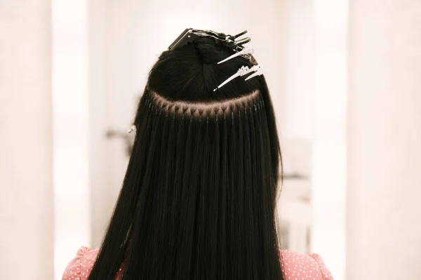 The hairdresser does hair extensions to a young girl in a beauty salon. Professional hair care. Close up of capsules and strands of grown hair