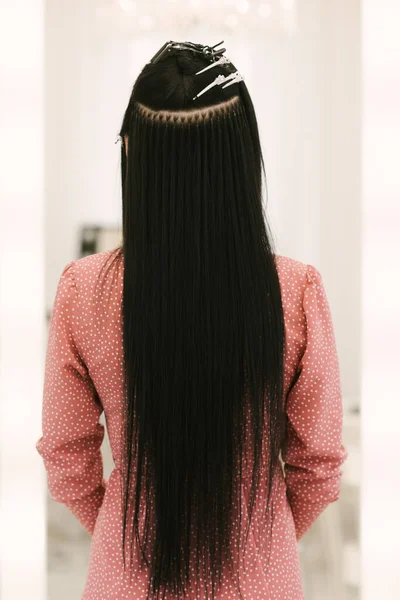 The hairdresser does hair extensions to a young girl in a beauty salon. Professional hair care. Close up of capsules and strands of grown hair