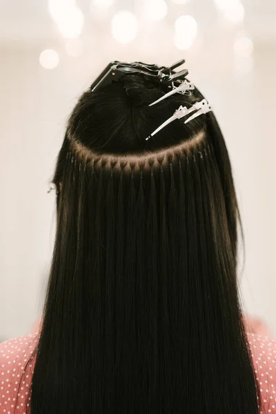 The hairdresser does hair extensions to a young girl in a beauty salon. Professional hair care. Close up of capsules and strands of grown hair