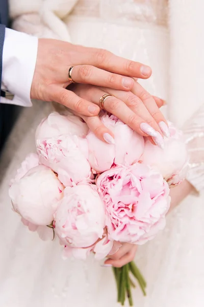 Beautiful wedding bouquet of pink peonies in the hands of the bride next to the groom.