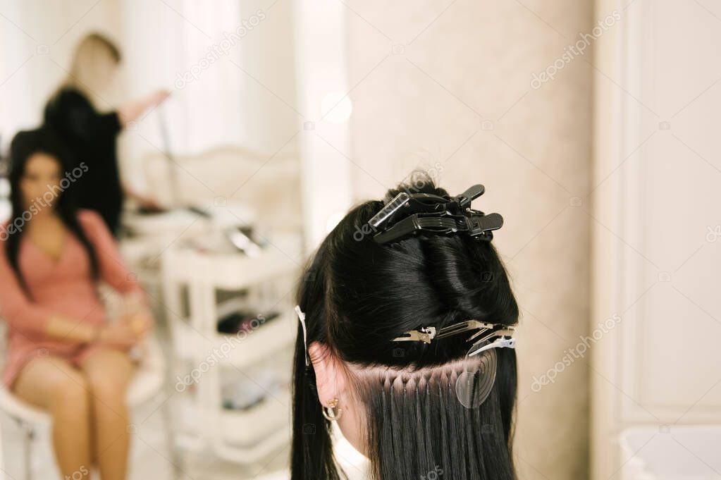 The hairdresser does hair extensions to a young girl in a beauty salon. Professional hair care.