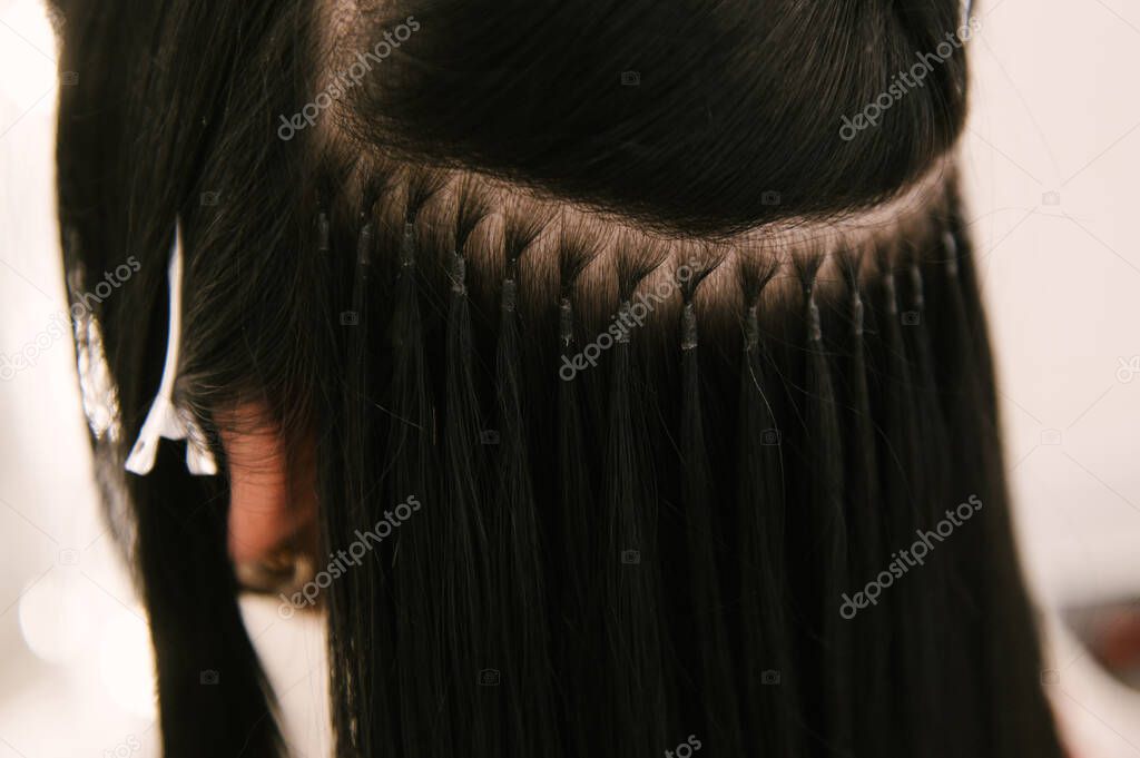 The hairdresser does hair extensions to a young girl in a beauty salon. Professional hair care. Close up of capsules and strands of grown hair