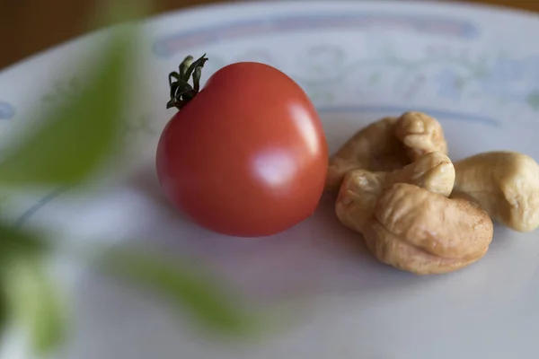 Pequeno tomate vermelho bonito ao lado de algumas nozes de caju . — Fotografia de Stock