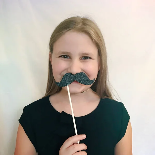 Menina com um bigode de papelão em um fundo branco — Fotografia de Stock
