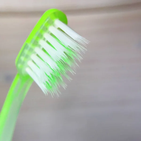 Escova de dentes verde close-up em um fundo de madeira leve — Fotografia de Stock