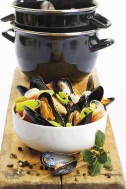 Mussels, rheinische art, with onions in a spicy sauce, in a porcelain dish in front of a mussel pot clipart