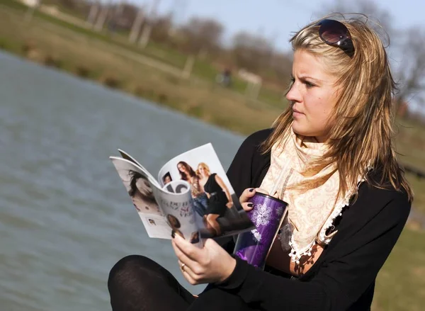 年轻的女人在湖边喝咖啡 翻阅杂志 — 图库照片