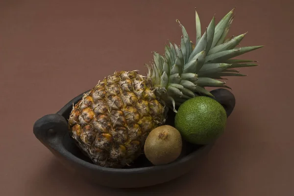 Pineapple, avocados and kiwi fruits in an archaic clay bowl