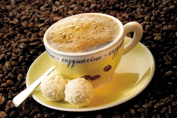 Cup of coffee with foam and coffee beans, plate with candies