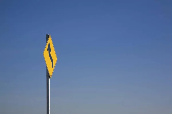 Sinal Trânsito Amarelo Com Uma Seta Curva Contra Céu Azul — Fotografia de Stock