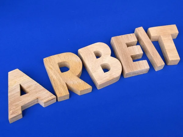Alphabet wooden letters on blue surface, German word of work, job