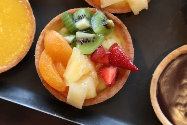 Koyu arka planda limon mousse ile çeşitli tropikal meyveler ve tartlets kaplı taze tatlı meyve tart
