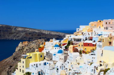 Santorini Peyzajı - Süper renkli Oia şehri panoramik manzaralı, mavi gökyüzü ve arka planda dağlar