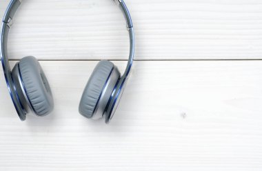 Beyaz ahşap arka planda müzik dinlemek için mavi ve gümüş kulaklıklar.
