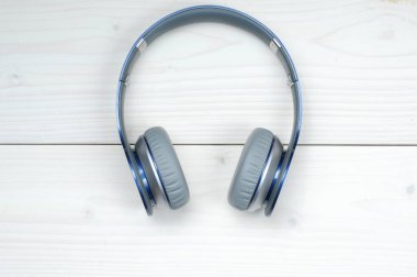 Beyaz ahşap arka planda müzik dinlemek için mavi ve gümüş kulaklıklar.