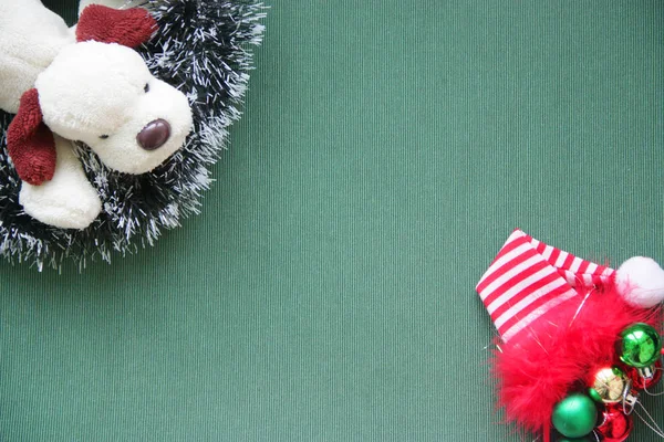 Πρωτοχρονιάτικα στολίδια, μπάλες, μια κόκκινη ΚΑΠ, έναs παιχνίδι σκύλοs σε πράσινο φόντο — Φωτογραφία Αρχείου