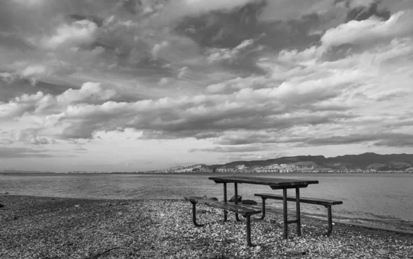 Wooden table near sea, sky and waves in background. Black and white landscape photo evoking loneliness. Incialti, Izmir, Turkey