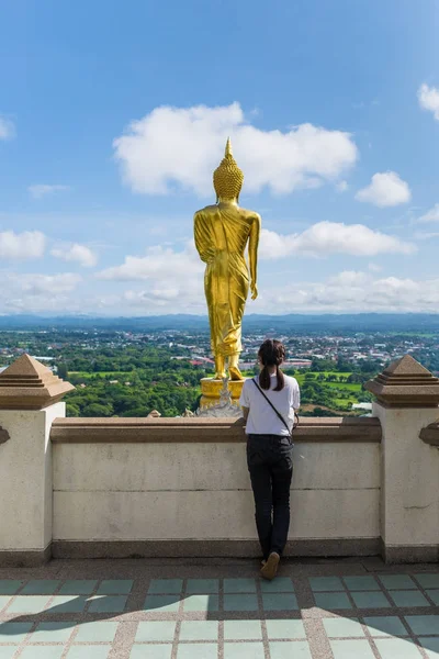 Kız beyaz gömlek ve siyah jean giyiyor. Sarı Buda geride duran ve Wat Prathat khao noi (genel Tapınağı) Nan il Tayland, sabah dağda evi aşağıda görmek