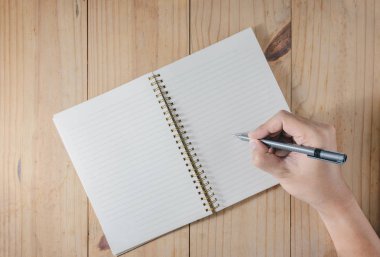Adamın elini ahşap masa üstünde beyaz defter üzerinde yazılı kalem kullanın