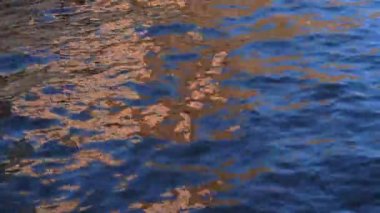 Suyun yüzeyi rüzgarda sallanıyor. Suyun üzerinde parlak renk yansımaları.